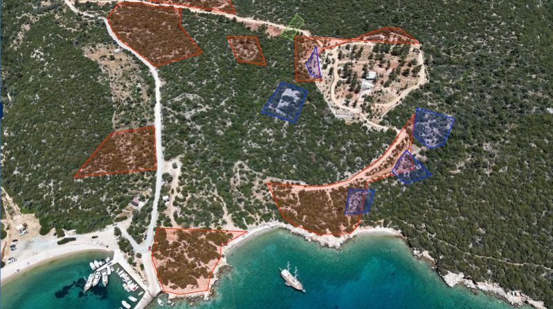 Drone ile çekilen fotoğrafta kırmızı ile işaretlenen yerler Milli Emlak arazileri belirtiyor. Mavi ile işaretlenen yerler ise Lelegler'den kalan tarihi yerleri gösteriyor. Yolun üzerindeki yeşil alan kapı konulduğu öne sürülen yeri işaret ediyor.